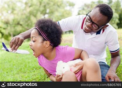 African American daughter playing airplane toy with father in outdoor green park