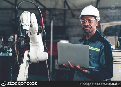 African American factory worker working with adept robotic arm in a workshop . Industry robot programming software for automated manufacturing technology .. African American factory worker working with adept robotic arm