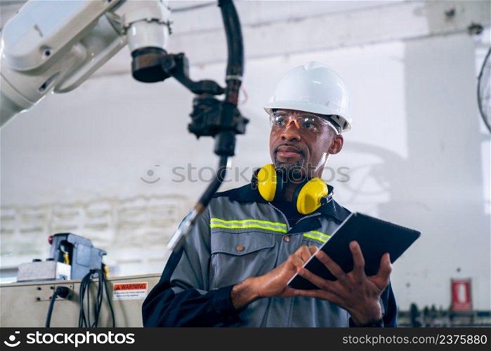 African American factory worker working with adept robotic arm in a workshop . Industry robot programming software for automated manufacturing technology .. African American factory worker working with adept robotic arm