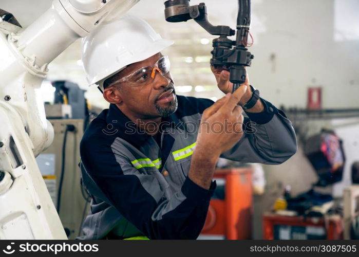 African American factory worker working with adept robotic arm in a workshop . Industry robot programming software for automated manufacturing technology .. African American factory worker working with adept robotic arm