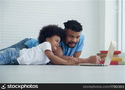 African American family father and little son lying on floor and online learning with laptop at home