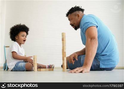 African American family father and little son playing building wooden blocks together on the floor at home