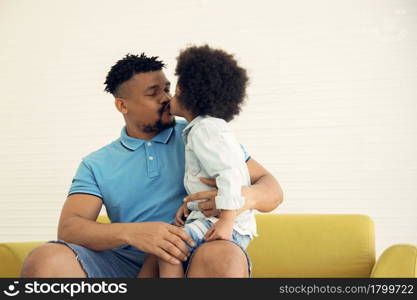 African American family little son kiss his young father at lip while sitting on sofa at home