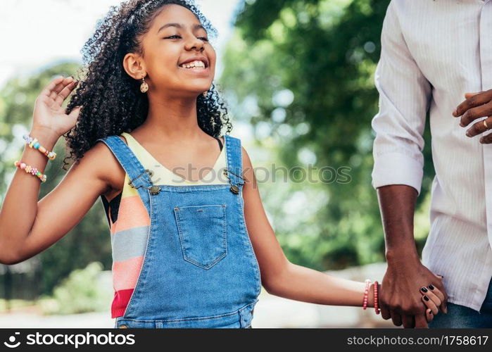 African American girl enjoying a day outdoors with her father while they hold hands and walk down the street.