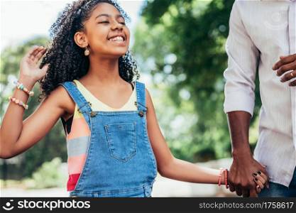 African American girl enjoying a day outdoors with her father while they hold hands and walk down the street.