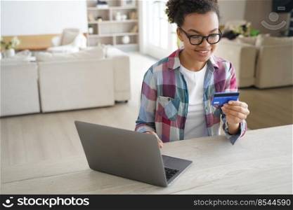 African american girl holding banking credit card, shopping purchasing online, using laptop, making payment. Smiling teen paying using e-bank service, sitting at desk at home. E-commerce.. African american teen girl holds banking credit card, shopping online at laptop at home. E commerce