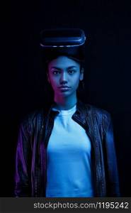 African-American girl in vr glasses with a virtual reality headset isolated on a black background, illuminated by neon lights