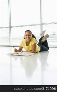 African American girl lying on floor doing homework looking up at viewer.