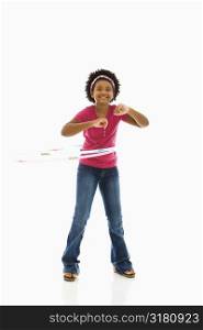 African American girl playing with hula hoop and smiling at viewer.