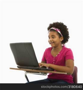 African American girl sitting in school desk typing on laptop computer.