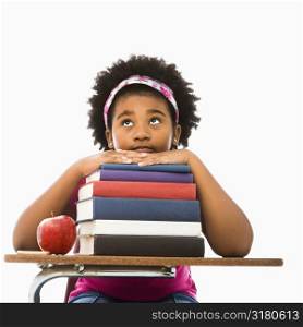 African American girl sitting in school desk with large stack of books looking bored.