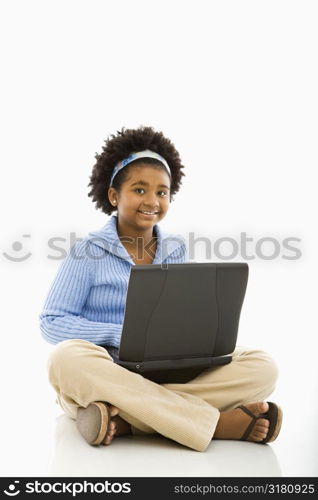 African American girl sitting on floor using laptop and smiling at viewer.