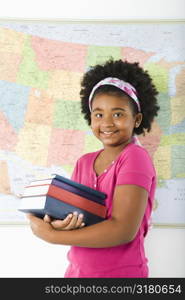 African American girl standing in front of USA map holding stack of books smiling at viewer.