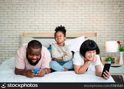 African American girls are not satisfied and sad, sitting in the middle between father and mother. Parents Are using the smartphone and abandoned children. Children need their parents attention.