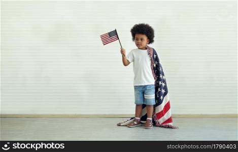 African American little boy holding small USA flag standing with us blanket on his shoulder at home