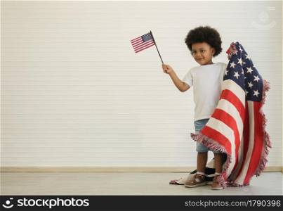 African American little boy holding small USA flags standing with us blanket on his shoulder, celebrating 4th July - Independence Day