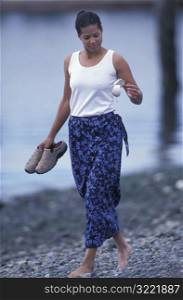 African American Looking At A Shell While Walking Along A Rocky Beach