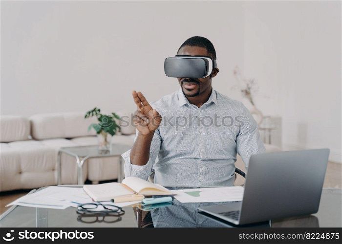 African american male architect designer wearing VR glasses works on interior project in virtual reality, sitting at office desk. Modern black guy using high tech gadget for working in cyberspace.. African american male architect designer in VR glasses works on interior project in virtual reality