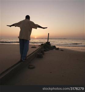 African American male balancing on beach erosion barrier at beach during sunset
