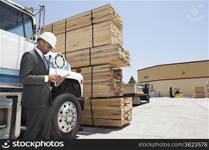 African American male contractor using tablet PC while standing by logging truck