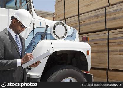 African American male contractor writing notes while standing by logging truck