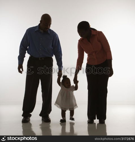 African American man and woman standing holding up infant girl by her hands against white background.