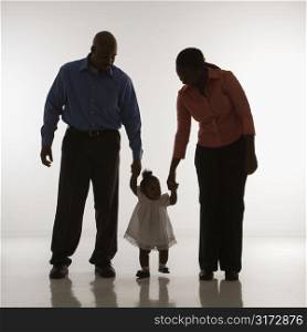 African American man and woman standing holding up infant girl by her hands against white background.
