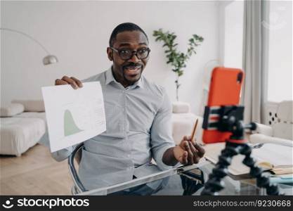 African american man economist showing data graph presenting to business partner via video call on smartphone. Black male businessperson coach discussing work project online with coworkers.. African american businessperson showing data graph to coworkers via video call online on smartphone