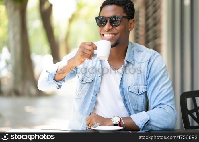 African american man enjoying and drinking a coffee while sitting at coffee shop outdoors. Urban concept.