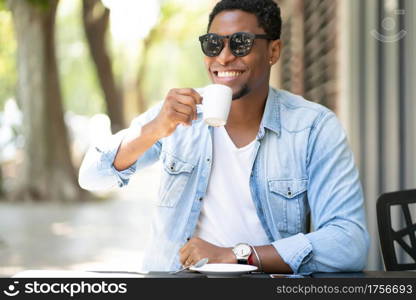 African american man enjoying and drinking a coffee while sitting at coffee shop outdoors. Urban concept.