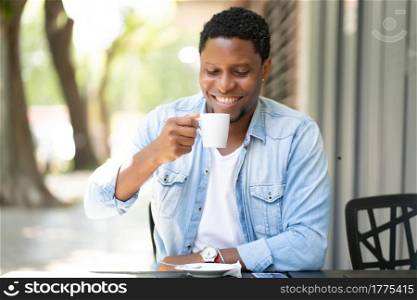 African american man enjoying and drinking a coffee while sitting at coffee shop outdoors. Urban concept.