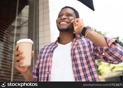 African american man holding a cup of coffee and talking on the phone while walking on the street. Urban concept.