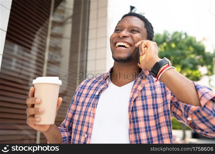 African american man holding a cup of coffee and talking on the phone while walking on the street. Urban concept.