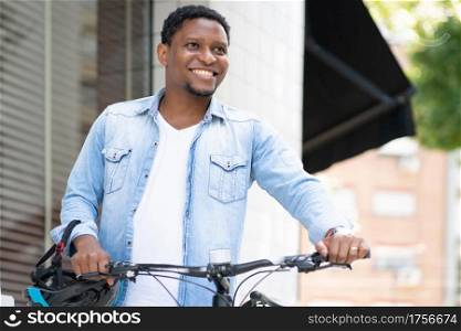 African American man holding a helmet on his hand while walking with a bicycle on the street.