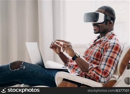 African american man in casual wear is businessman. Guy in vr headset at home office. Relaxed freelancer sitting in cosy chair and working on project on pc. High tech digital technology and vr gaming.. African american man in casual wear is businessman. Guy in vr headset at home office.