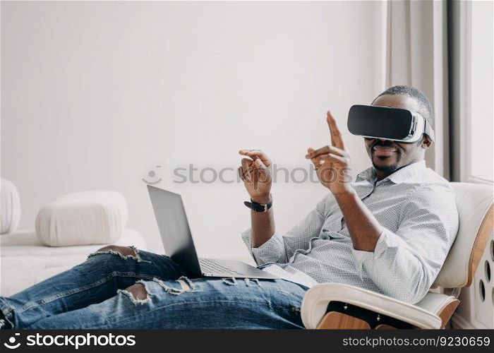 African american man in vr goggles is working at home. Relaxed businessman clicks virtual buttons. Distant work and futuristic gaming. Modern digital technology for business and creativity.. African american man in vr goggles is working at home. Relaxed businessman clicks virtual buttons.