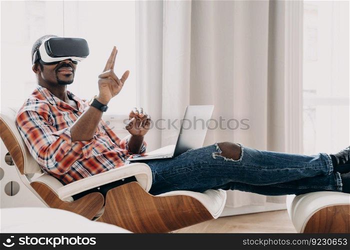 African american man in vr headset enjoying the vision at home office. Businessman has virtual meeting. Relaxed freelancer is sitting in chair and working on project. High tech digital technology.. African freelancer in vr headset enjoying the vision at home. Businessman has virtual meeting.