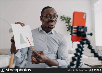 African american man showing chart to business partner by video call using smartphone. Black male business analyst shows a client or colleague economic graph, analyzes business data online.. African american business analyst shows economic graph to coworkers online by video call with phone