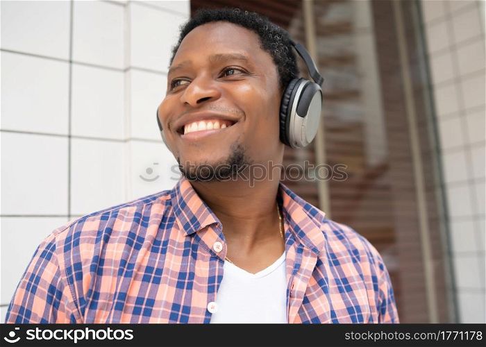 African american man smiling and listening music with headphones while standing outdoors on the street.