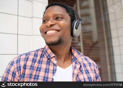 African american man smiling and listening music with headphones while standing outdoors on the street.