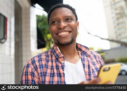 African american man smiling and using his mobile phone while standing outdoors on the street. Urban concept.