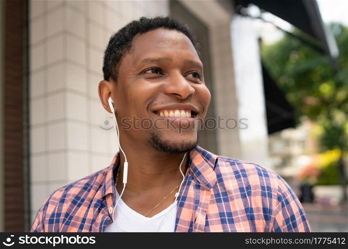 African american man smiling while listening music with earphones outdoors on the street. Urban concept.