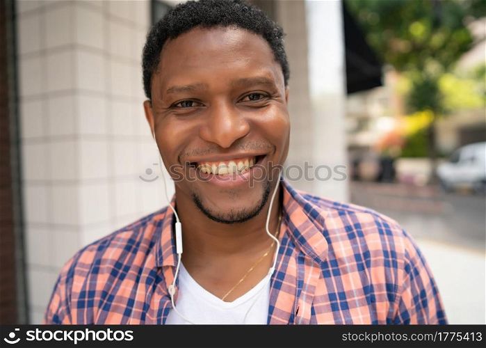 African american man smiling while listening music with earphones outdoors on the street. Urban concept.