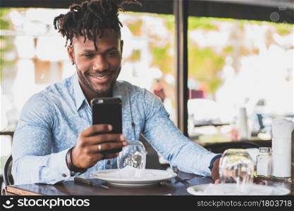 African American man smiling while using a mobile phone at a restaurant.
