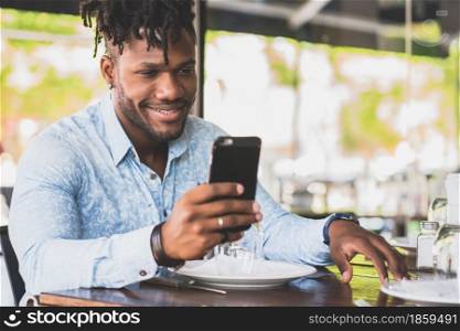 African American man smiling while using a mobile phone at a restaurant.