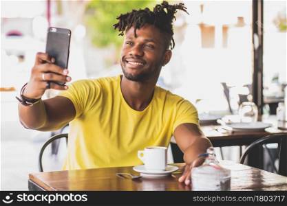 African American man taking a selfie with a mobile phone while sitting at a coffee shop.