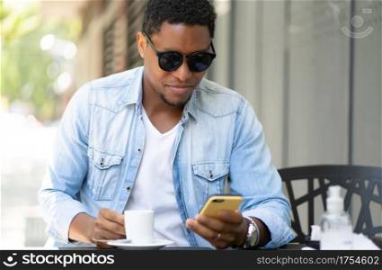 African american man using his mobile phone while sitting at a coffee shop. Urban concept.