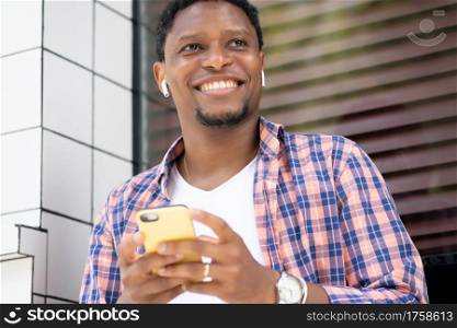 African american man using his mobile phone while sitting at a store window on the street. Urban concept.