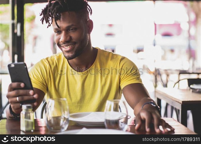 African american man using his mobile phone while sitting in a restaurant.