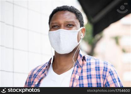 African american man wearing a face mask while listening music with earphones outdoors on the street. New normal lifestyle concept.